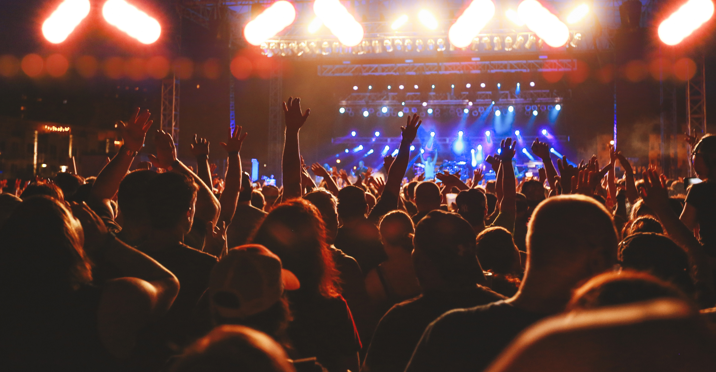 Concert crowd cheering, concert audience arms raised. Live entertainment concept of music festival crowd cheering for live music performance, rock music concert event, or enthusiast fans enjoying nightlife. Rear view concert crow, audience with concert lights and stage background