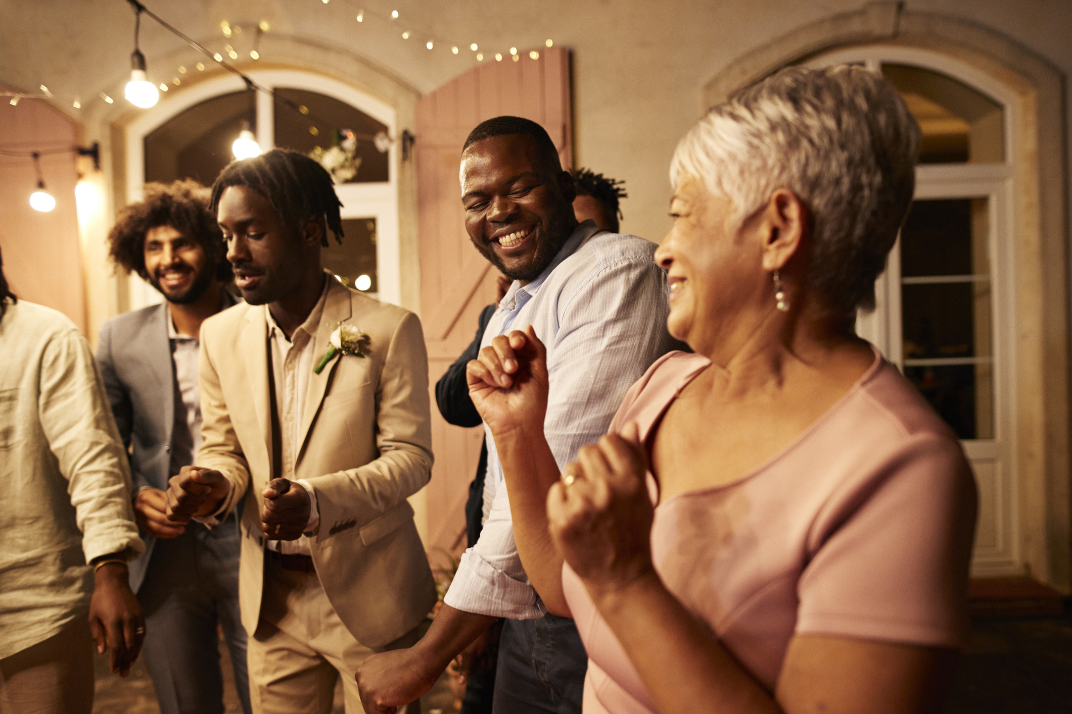 Happy senior woman dancing with male guests and groom at wedding reception party